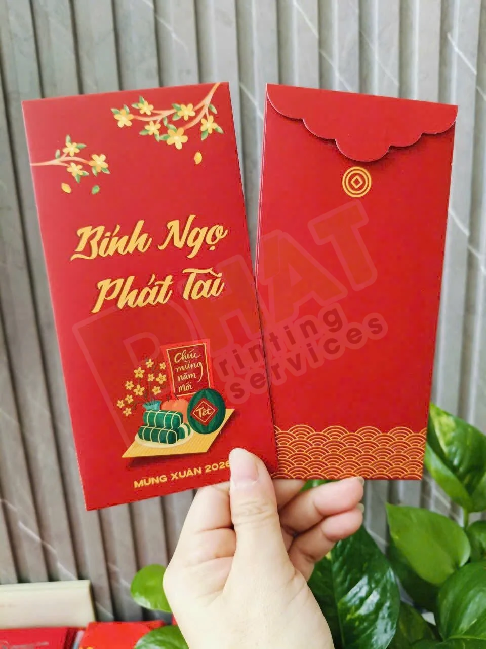 Tay cầm hai bao lì xì nền đỏ in chữ chúc Tết màu vàng, mặt trước và mặt sau có nắp gấp