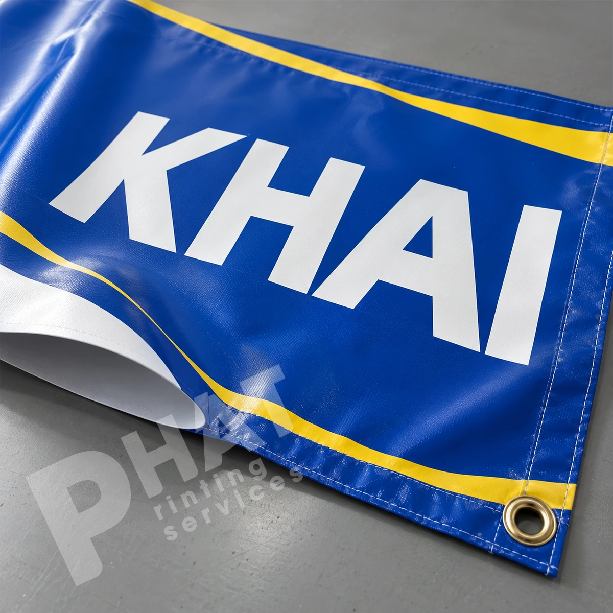 Ảnh render minh họa cận chữ KHAI màu trắng trên banner xanh, mép may và khoen kim loại ở góc tấm