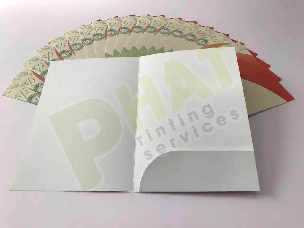 File In Folder: Dàn Trang Trên Khuôn Bế, Tai Gài Và Khe Name Card 1 Folder kẹp hồ sơ mở phẳng, mặt trong màu trắng có tai gài bo cong, phía sau là nhiều folder in màu