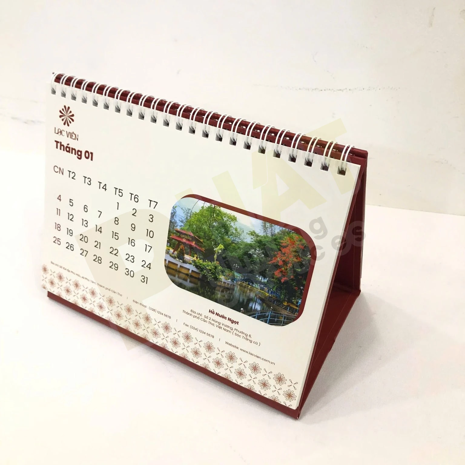 Lịch để bàn lò xo đế gập màu đỏ đô, trang tháng có bảng ngày và ảnh phong cảnh