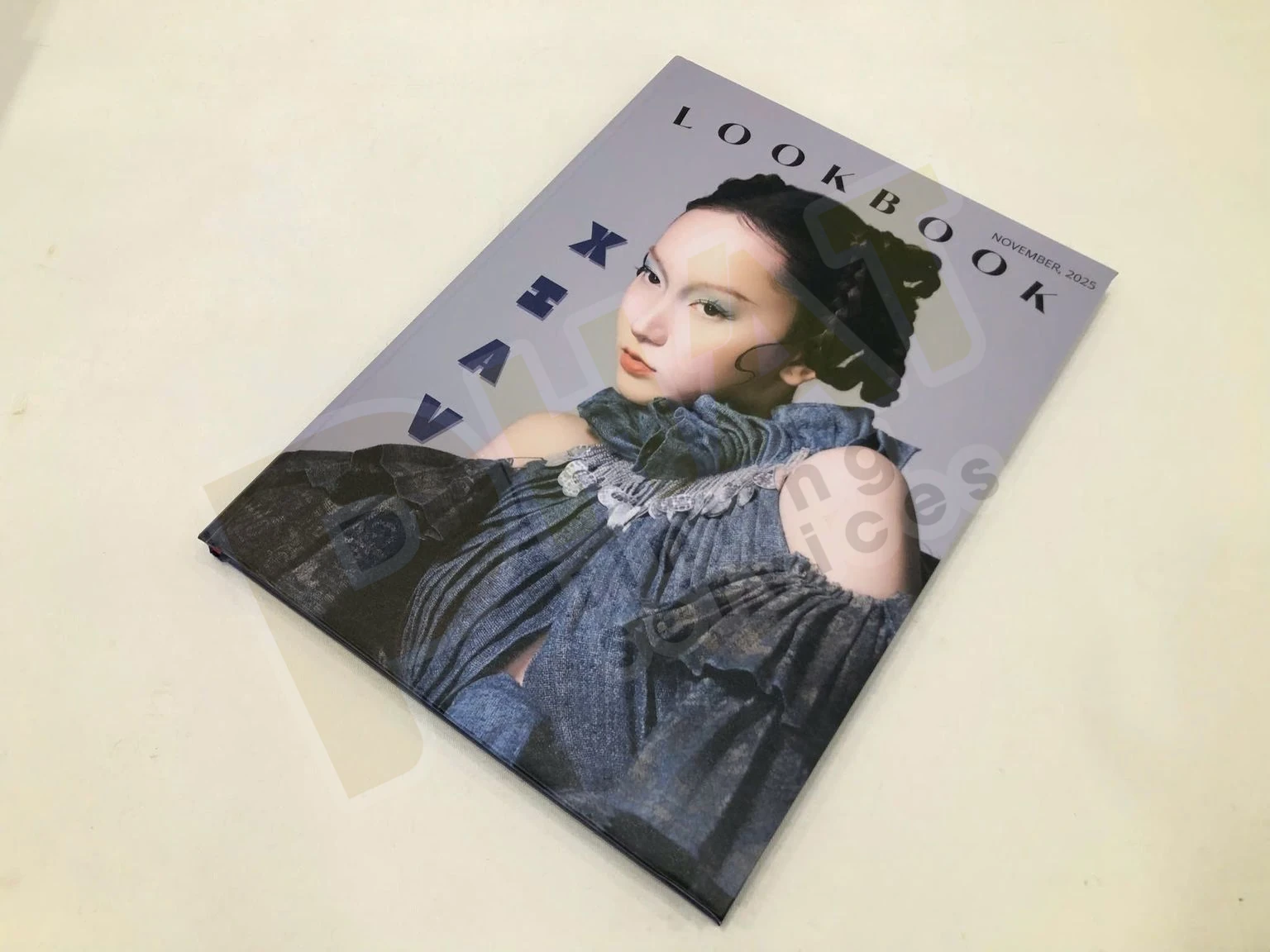 Cuốn lookbook bìa cứng in ảnh chân dung người mẫu mặc áo vải denim, đặt nghiêng trên bàn