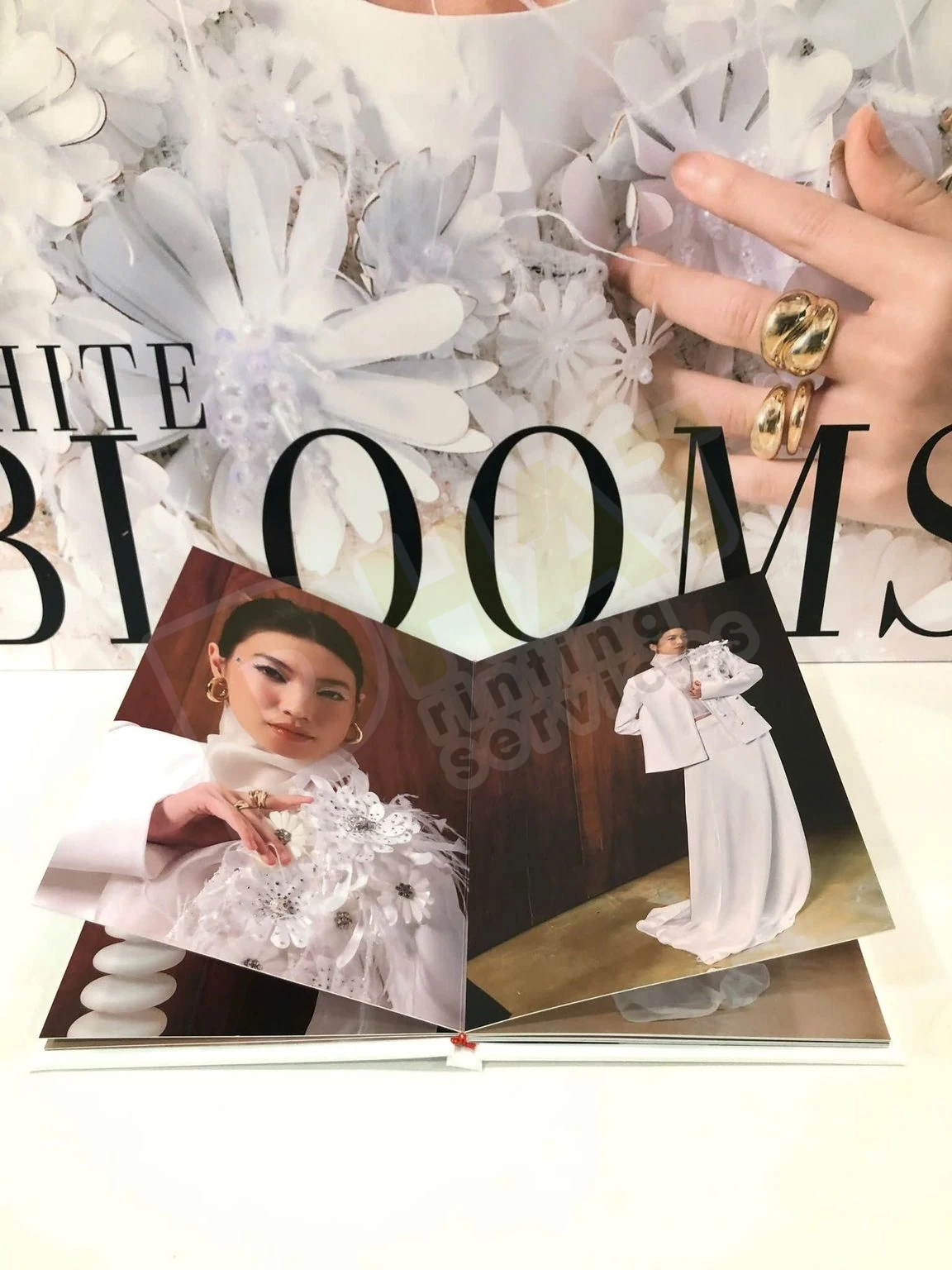 Cuốn photobook bìa cứng mở phẳng hai trang ảnh, phía sau là bối cảnh hoa giấy trắng