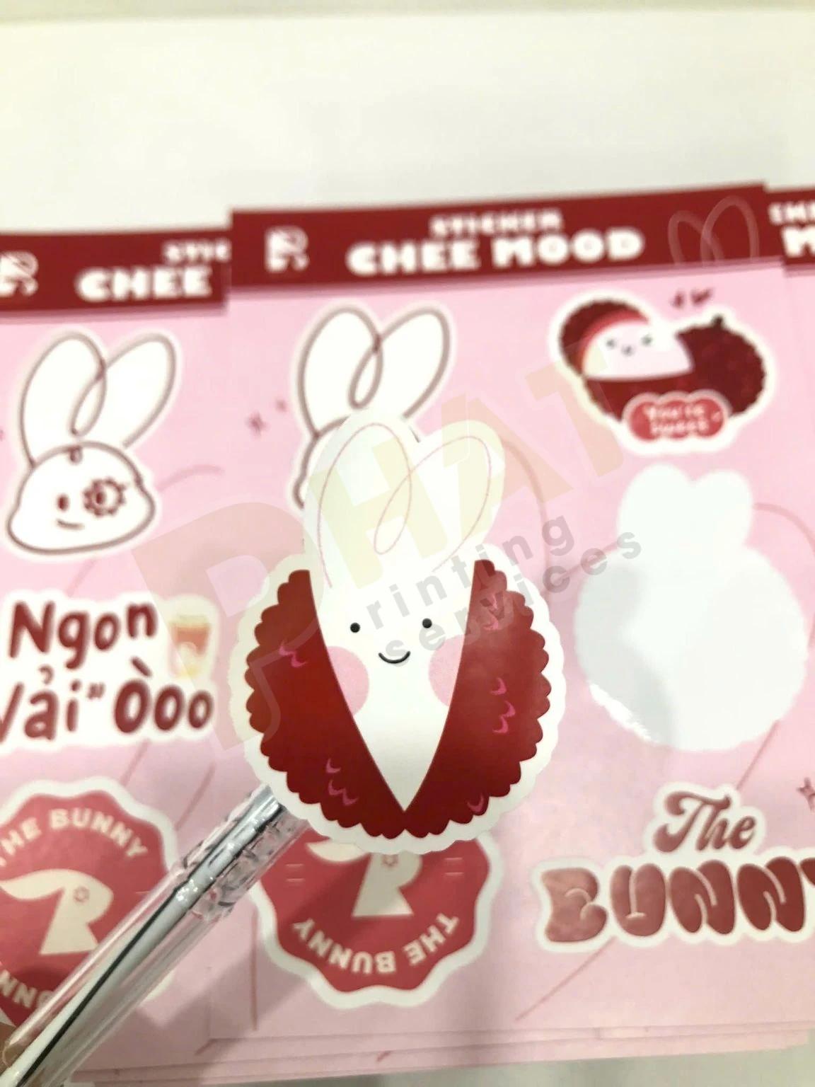 Ấn Phẩm Gói Hàng Shop Online: Bộ Tag, Sticker, Thank You Card 3 Cận cảnh một sticker hình nhân vật được nhấc khỏi tờ sticker nền hồng bằng đầu bút