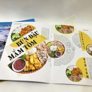 Cuốn tạp chí in màu mở ra ở trang đôi có ảnh món ăn và các cột chữ