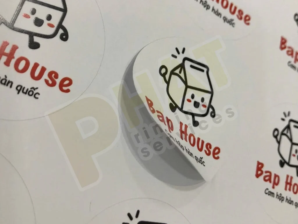 Tờ tem nhãn tròn in logo đỏ đen, một con tem đang được bóc lên khỏi lớp đế