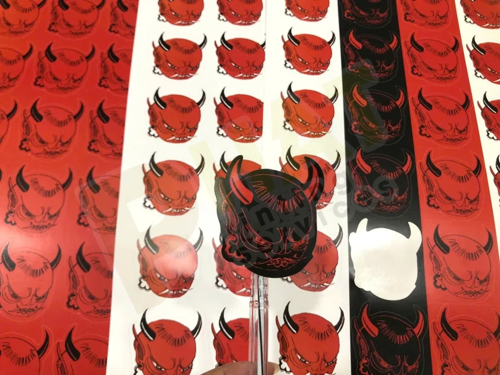 Nhiều tờ decal in hình mặt quỷ đỏ đen, một hình đã bóc thấy phần đế trắng
